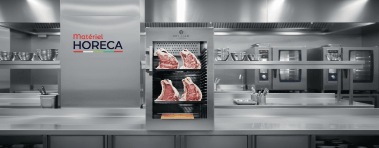 Armoire de maturation Dry Ager DX0500 Premium S posée sur un plan de travail, éclairage studio, grandes pièces de viande apparentes.