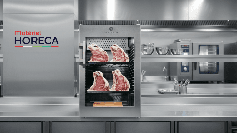 Armoire de maturation Dry Ager DX0500 Premium S posée sur un plan de travail, éclairage studio, grandes pièces de viande apparentes.