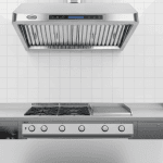 Hotte aspirante 1200 mm installée dans une cuisine professionnelle animée, acier inoxydable sous éclairage intense et ambiance de service.