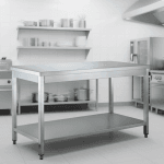 Chef en cuisine professionnelle utilisant une table inox avec sous-tablette, ambiance moderne et énergique